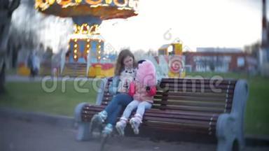 美丽的小女孩坐在游乐园的长凳上，吃着滚<strong>滑</strong>轮<strong>滑冰鞋</strong>上滚来滚去的粉红色甜棉糖